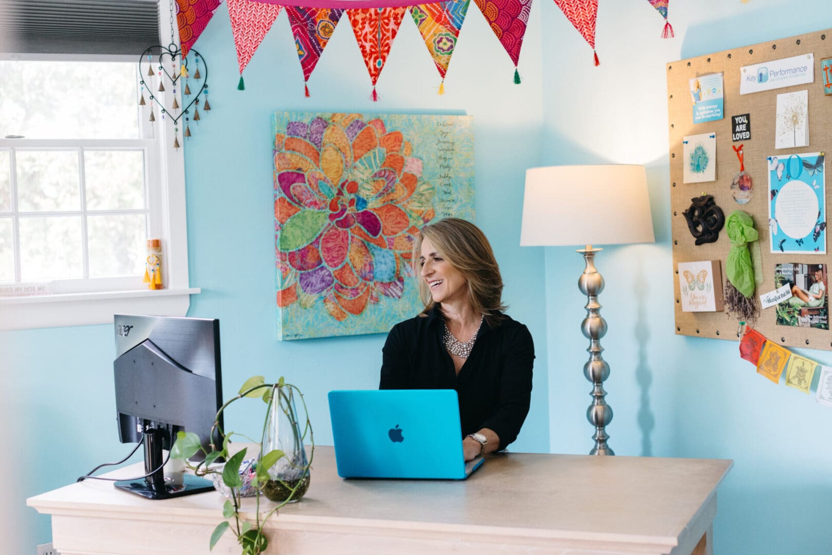 Woman working happily at a desk with a laptop and colorful decor.